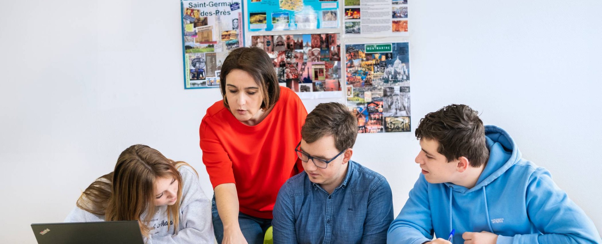 Twee studenten kijken lachend naar hun docent die tegenover hen zit.